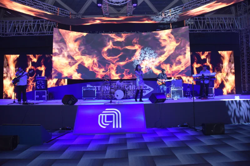 Live band performing on a large corporate event stage featuring a dynamic fire graphic on the LED screen backdrop.