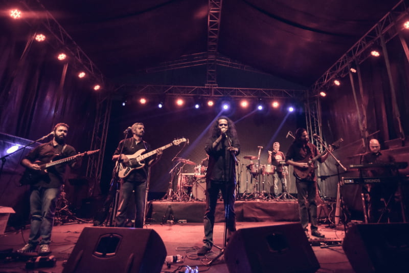 Rock band performing on stage during a night concert illuminated by dramatic purple stage lights.